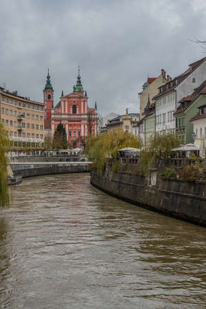 Picturesque buildings along Ljubljanica river on a dull autumn november day. Lazy gray day in Ljubljana, Slovenia, with dirty brown river flowing under the bridge.の写真素材