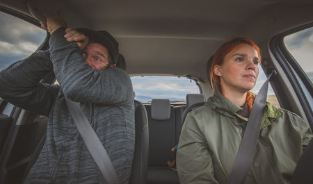 A woman is calmly driving a car and a man in the next seat is scared as hell. Totally scared...