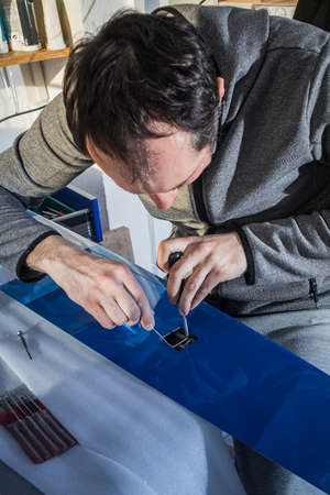 A person with tools assembling a servo RC motor in a wing of an aeroplane model. Wing in a blue color, connector wires and tools seen in the background.の写真素材