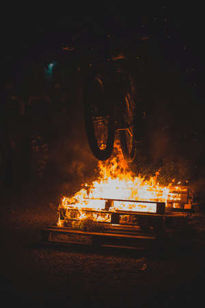 Totally crazy cyclist on a mountain bike riding through bonfire, sparks and flames whooshing past the biker in a real event. Biker dangerously playing with open fire.の写真素材