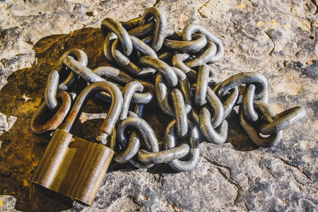A golden padlock and silver chain showing signs of wear in a rocky bacground.の写真素材
