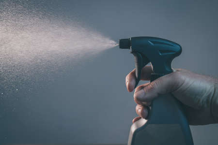 Bare hand holding a spray bottle for cleaning and operating it. Drops from bottle are being sprayed all over the place. Side view of an operational plastic spray bottle.の写真素材