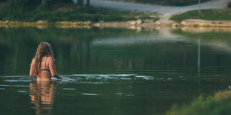 Young woman in a bikini bathing in a green cold lake.の写真素材