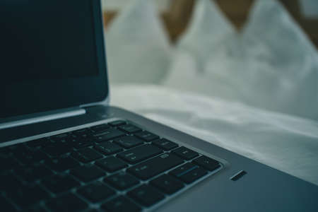 Detail view of a laptop keyboard sitting on a bed in hotel room. Vintage hotel room with laptop on the sheet. Concept of online hotel booking.の写真素材