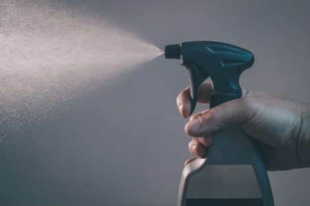 Bare hand holding a spray bottle for cleaning and operating it. Drops from bottle are being sprayed all over the place. Side view of an operational plastic spray bottle.の写真素材