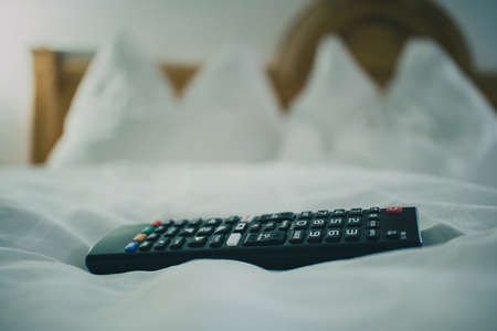 Modern television remote on a bed in a hotel. Wooden hotel room bed with pillows and headbord in the background. Concept of TV enjoyment in the hotel room.の写真素材