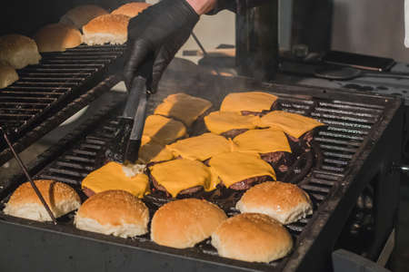 Preparing cheese burgers or hamburgers with bread buns on a hot coal grill outside. Detail of delitious juicy home made burgers.の写真素材