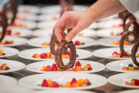 A person's hand is visible preparing and decorating a dessert made out of chocolate and fruit on a...
