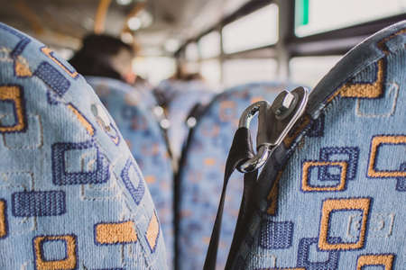 Detail of an upper seatbelt anchoring point on a public bus with some passengers in the background. Public transportation with unused safety options such as seatbelt.の写真素材