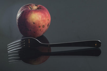 A natural looking red apple on a shiny reflective surface accompanied by a fork. Concept of healthy...