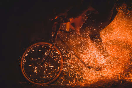 Totally crazy cyclist on a mountain bike riding through bonfire, sparks and flames whooshing past the biker in a real event. Biker dangerously playing with open fire.の写真素材