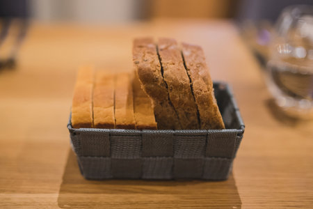 Slices of two different bread types in a grey woven basket on a wooden table. Fancy serving of bread slices  in shallow depth of field, focus on bread crust.の写真素材