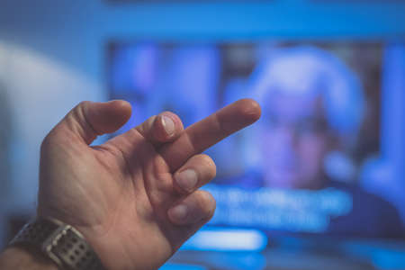Showing fuck you sign with a hand towards the television. Concept of not liking the television programme.の写真素材