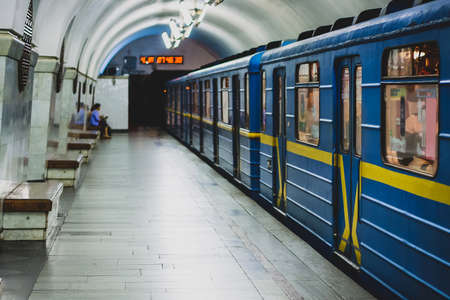 A metro or underground train in blue and yellow color is departing a metro station in Kiev, Ukraine. One passenger is seen on the platform.の写真素材