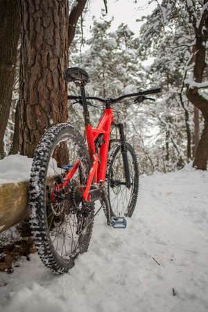 Enduro 27,5 mountain bike in red color resting on a bike single track on a cold snowy winter day. Concept of extreme sports or mountain biking in cold and snowy weather. Outdoor in winter.の写真素材