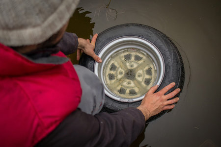 A mechanic is testng a car wheel for air leak with submerging or diving it into a pool of water and...