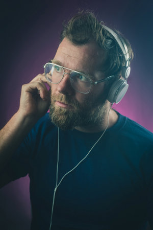 Portrait of a hipster looking man on a purple gradient background with white headphones. One hand is on the headphone.の写真素材