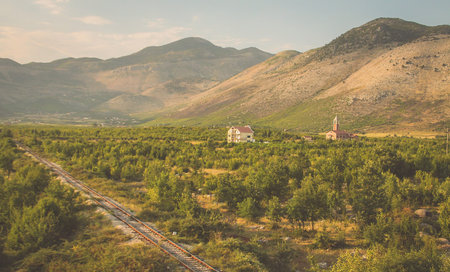A lone single track railway line crossing the fields and plains with some mountains and houses seen...
