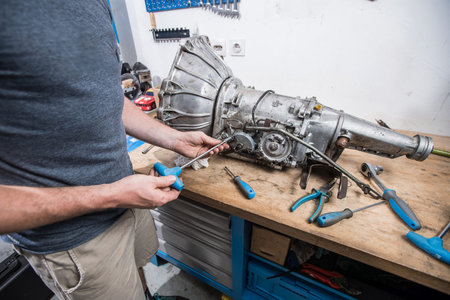 Young caucasian male is seen wrenching an automatic gearbox of an old vintage car. Tune up or...