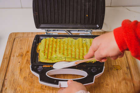 Woman making or preparing an avocado omlette in a toaster. Good delicious LCHF style food made from avocado base, roasted in a grill toaster. Fresh healthy good food.の写真素材