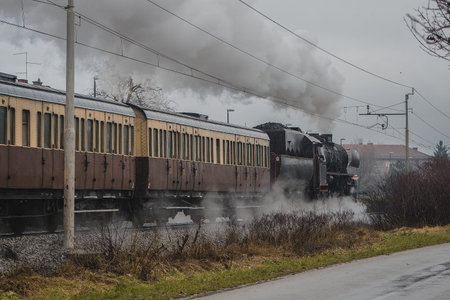 Old vintage steam train with black locomotive is running full power on a railroad track in the city...