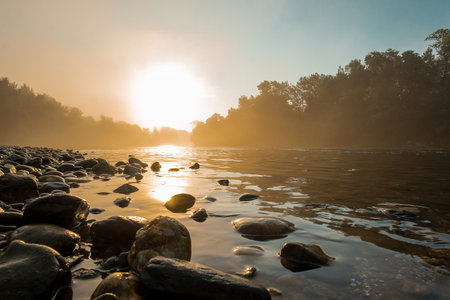 Misty hazy panorama of a river and riverbank with cobblestones in early morning hours. Mystical setting during an early morning time.の写真素材