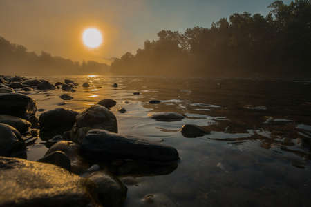 Misty hazy panorama of a river and riverbank with cobblestones in early morning hours. Mystical setting during an early morning time.の写真素材