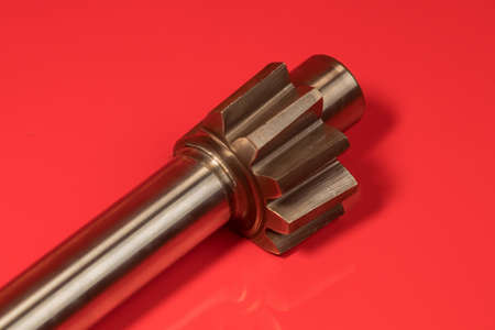 Detail or close up of a chrome axle with teeth as used in the power steering junction. Axle on a red shiny surface.の写真素材