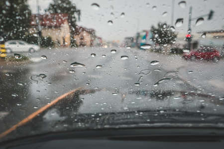 Rain drops on a car windshield obstructing the view of the junction and red light. Dangerous situation on the road because of wet and dirty windscreenの写真素材