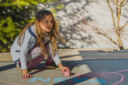 Little blonde girl squatting on the floor and drawing a picture with a pink piece of chalk. Creative leasure  time for kids while celebrating birthday.の写真素材
