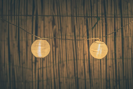 Two round paper lanterns in a home garden on a wooden thatched background at night. Festive...