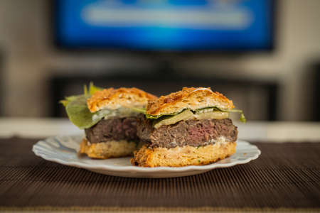 LCHF Low carbohydrate high fat burger or hamburger meal. LCHF burger with non carbohydrate bread made of sesame, eggs, chees, almonds. Concept picture of a LCHF burger in front of television screen.の写真素材