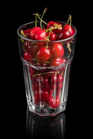 A bunch of fresh red cherries in a glass, isolated on a black background with a reflection on the ground.の写真素材