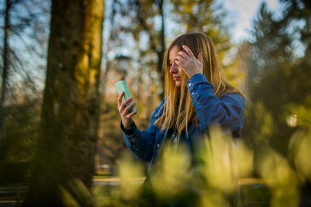 Cute blonde girl with long hair, septum piercing and jeans shirt using her telephone as a mirror in...