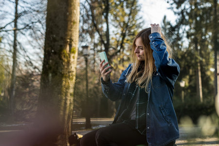 Cute blonde girl with long hair, septum piercing and jeans shirt using her telephone as a mirror in...