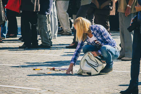 Young woman dropped a white purse and all contents have dropped on the floor. Woman picking up contents of purse or a bag in a crowd.の写真素材