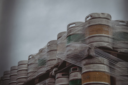 Large amount of aluminium beer kegs stacked on each other with euro palettes and wrapped around with...
