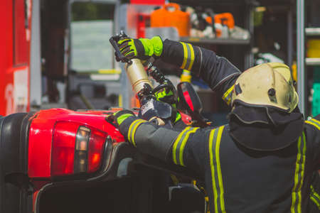 Firefighters using a hydraulic jaws of life or scissors to cut the crashed car open to save the driver caught inside. Emergency situation in a road crashの写真素材