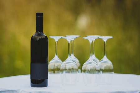A bottle of wine with a set of glasses on a table in front of a green outdoor background.の写真素材