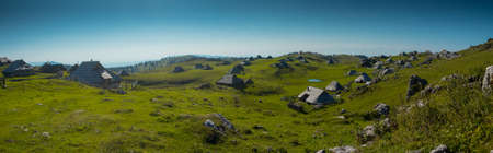 Wide panorama of typical wooden houses or cottages on the Velika planina plateau in Slovenia on a hot sunny summer day with clear blue skies.の写真素材
