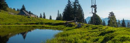 Wide panorama of typical wooden houses or cottages on the Velika planina or Mala Planina plateau in Slovenia on a hot sunny summer day with clear blue skies and lush green grass.