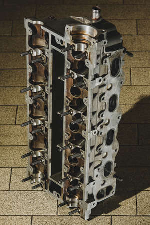 A 16V aluminium cylinder head on the floor with brown tiles, like in a workshop or similar place.の写真素材
