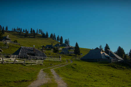 Panorama of typical wooden houses or cottages on the Velika planina or Mala Planina plateau in Slovenia on a hot sunny summer day with clear blue skies and lush green grass.の写真素材