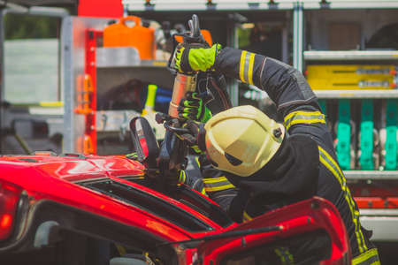Firefighters using a hydraulic jaws of life or scissors to cut the crashed car open to save the driver caught inside. Emergency situation in a road crashの写真素材