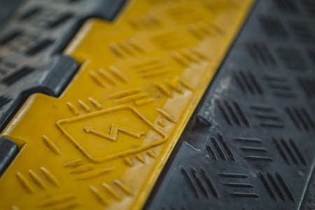 Black and yellow plastic cable protector on the ground. Floor cable protector with plastic cover. Cable saver on an event in high visibility colors.の写真素材
