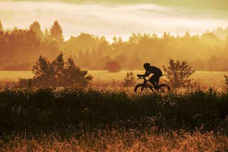 Silhouette of a professional road cyclist in an early morning, with haze and fog rising due to sun coming up.の写真素材