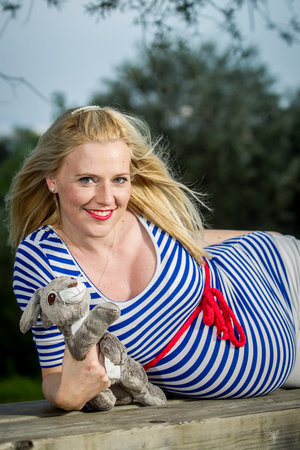 A cute pregnant girl with a striped top laying on a bench holding a fluffy bunny toy.の写真素材