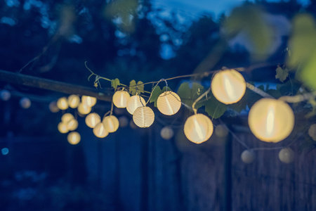 Row of round paper lanterns in a home garden on a wooden thatched background at night. Festive...