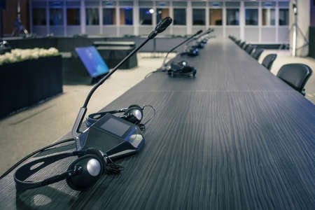 A row of microphone and headphone sets for speech and translation on a business or congress meeting on a desk. Translation booths are seen in the background.の写真素材