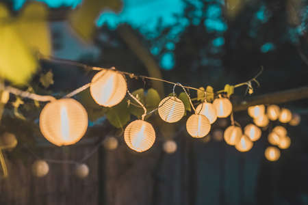 Row of round paper lanterns in a home garden on a wooden thatched background at night. Festive decoration in the garden on an evening.の写真素材
